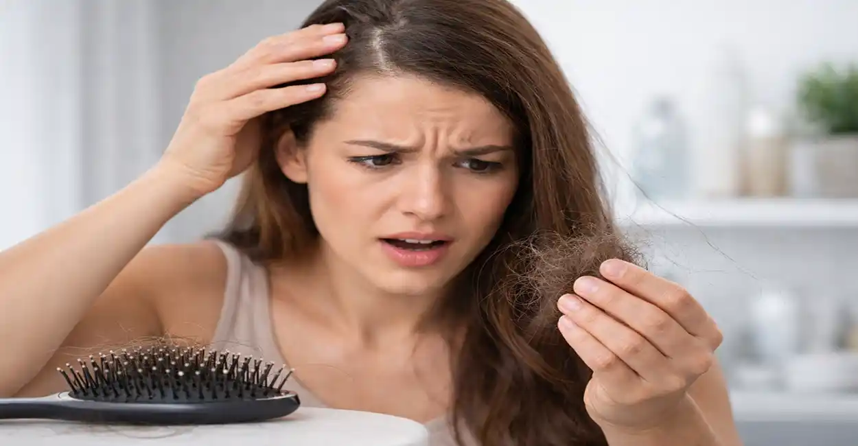 Mulher preocupada segurando fios de cabelo caindo enquanto analisa queda de cabelo no banheiro